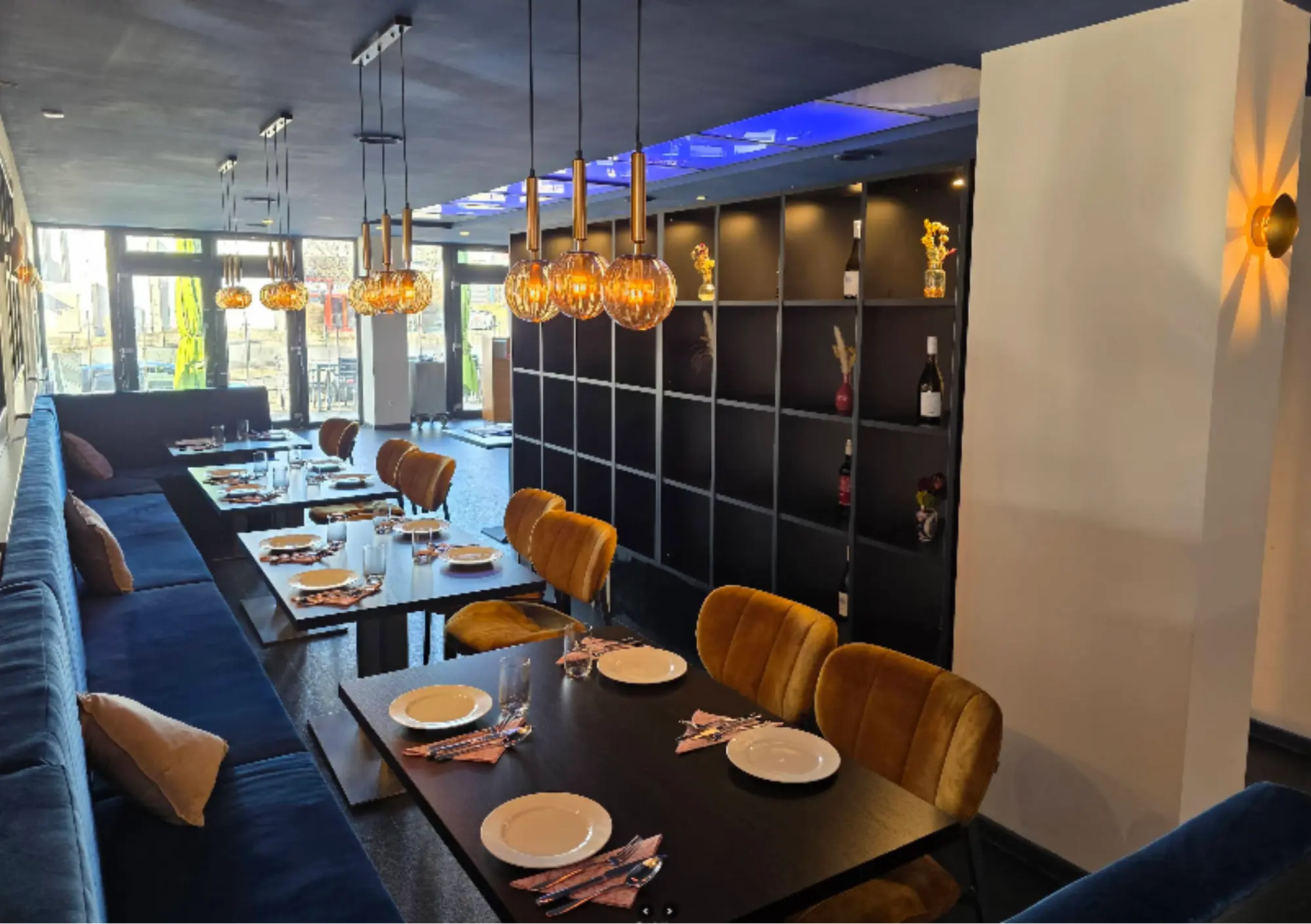 Stilvoller Gastraum mit blauen Sitzbänken, Samtstühlen und Weinregal im Blue Feathers Kaiserslautern