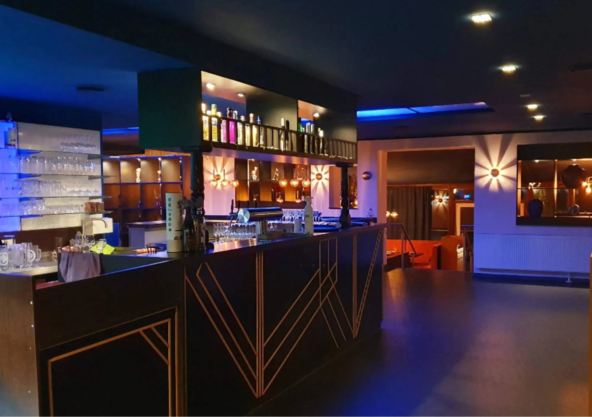 Stilvolle Bar mit goldenem Art-déco-Tresen und beleuchteten Regalen im Blue Feathers Kaiserslautern